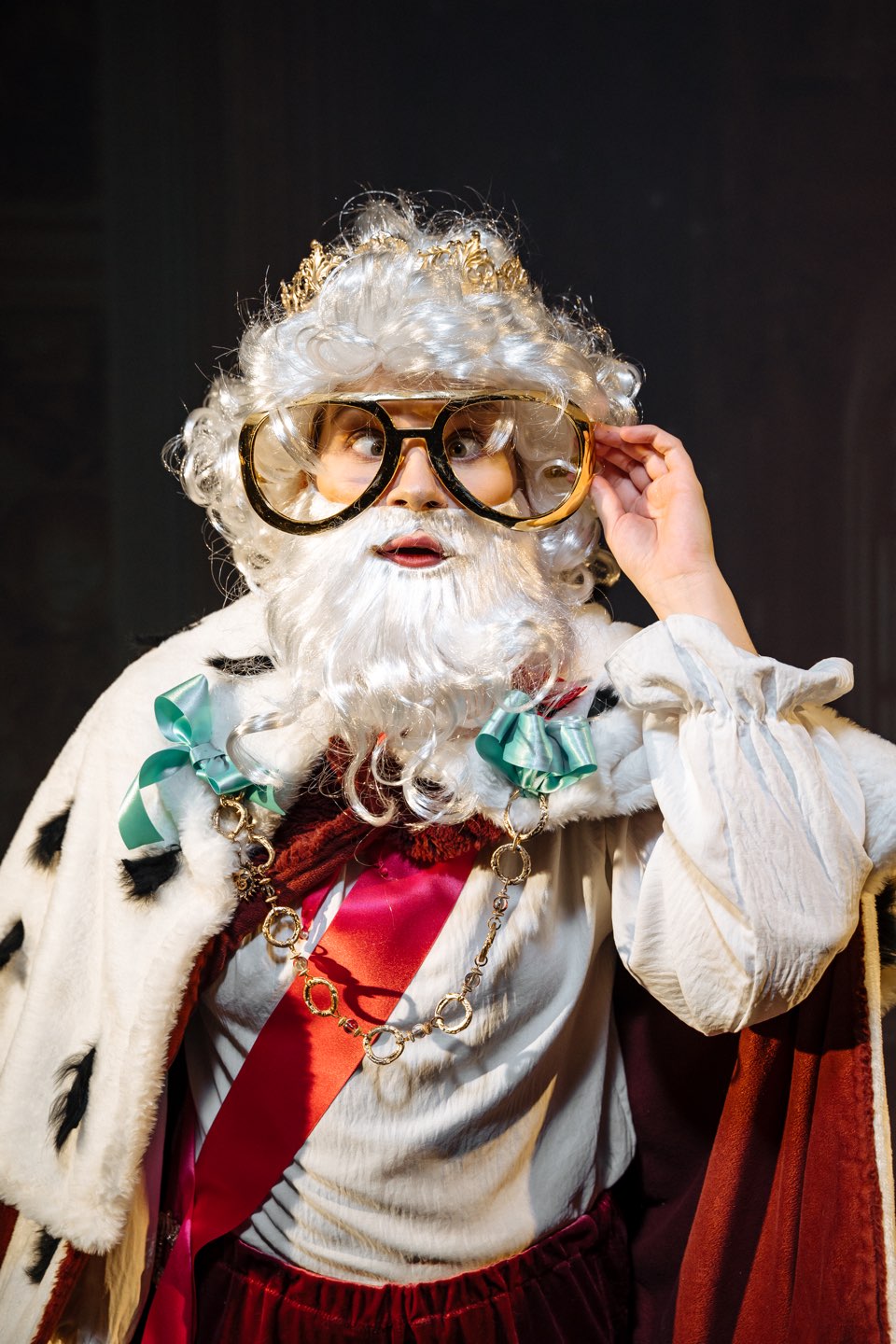 The King in an ermine robe and a crown adjusting his large glasses
