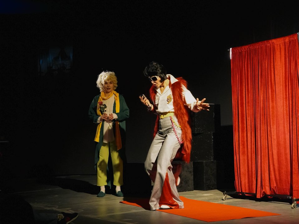 The Little Prince watching a showman in a sequined suit on a red carpet