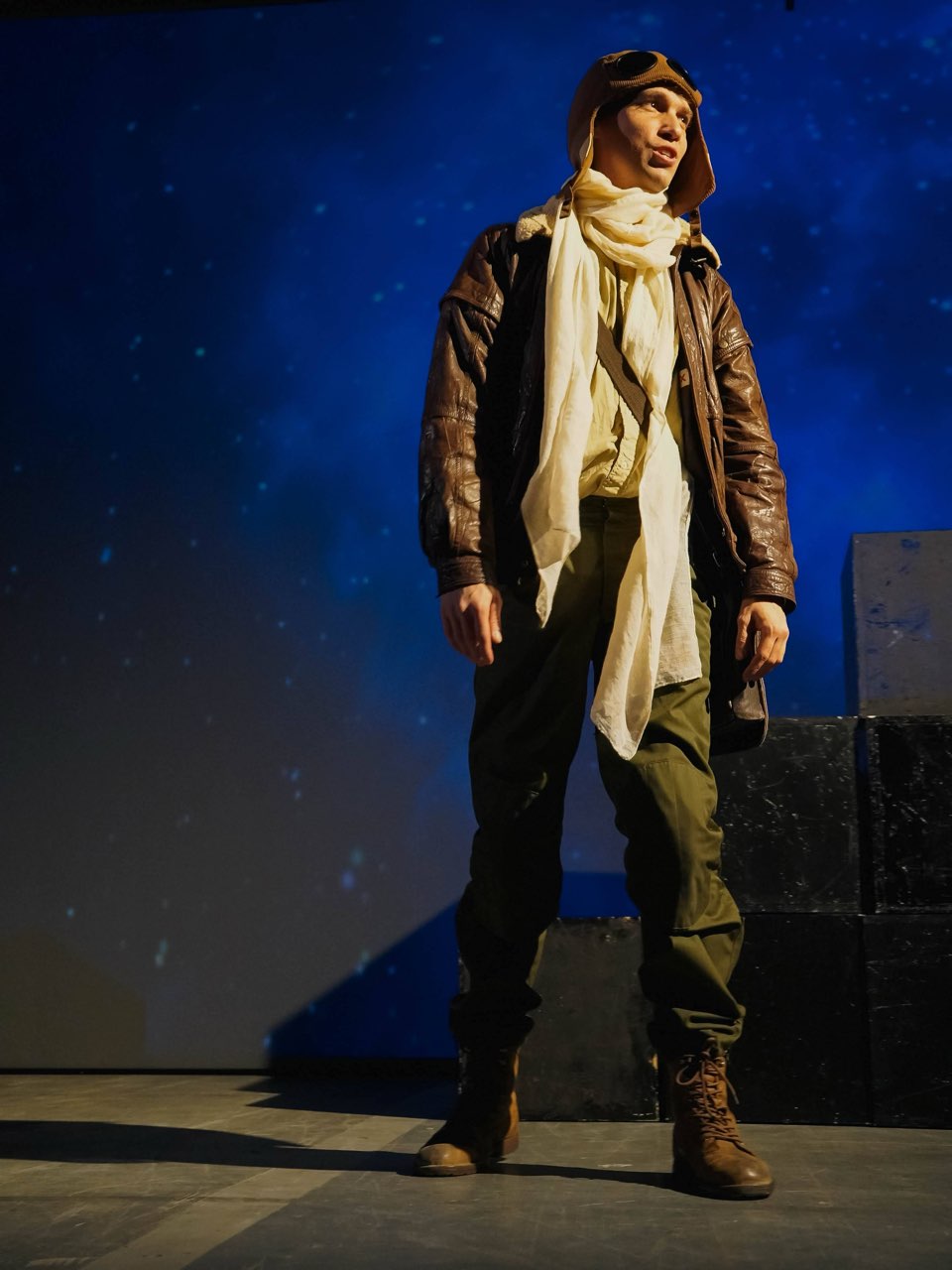 The Pilot in a leather jacket and a white scarf against a starry blue backdrop