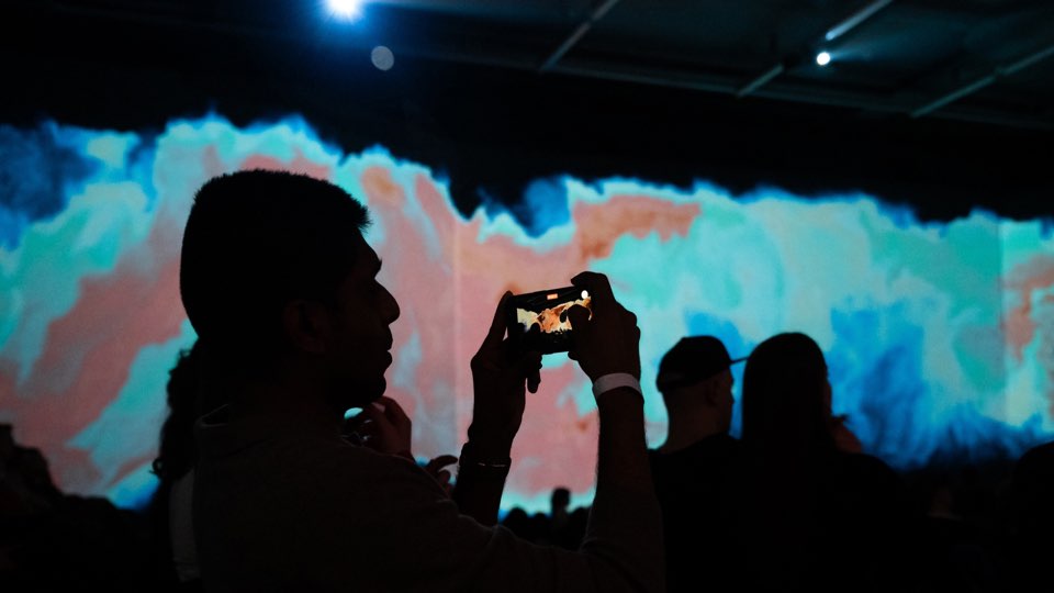 Bezoeker fotografeert de projecties met een telefoon in Vincent Hall